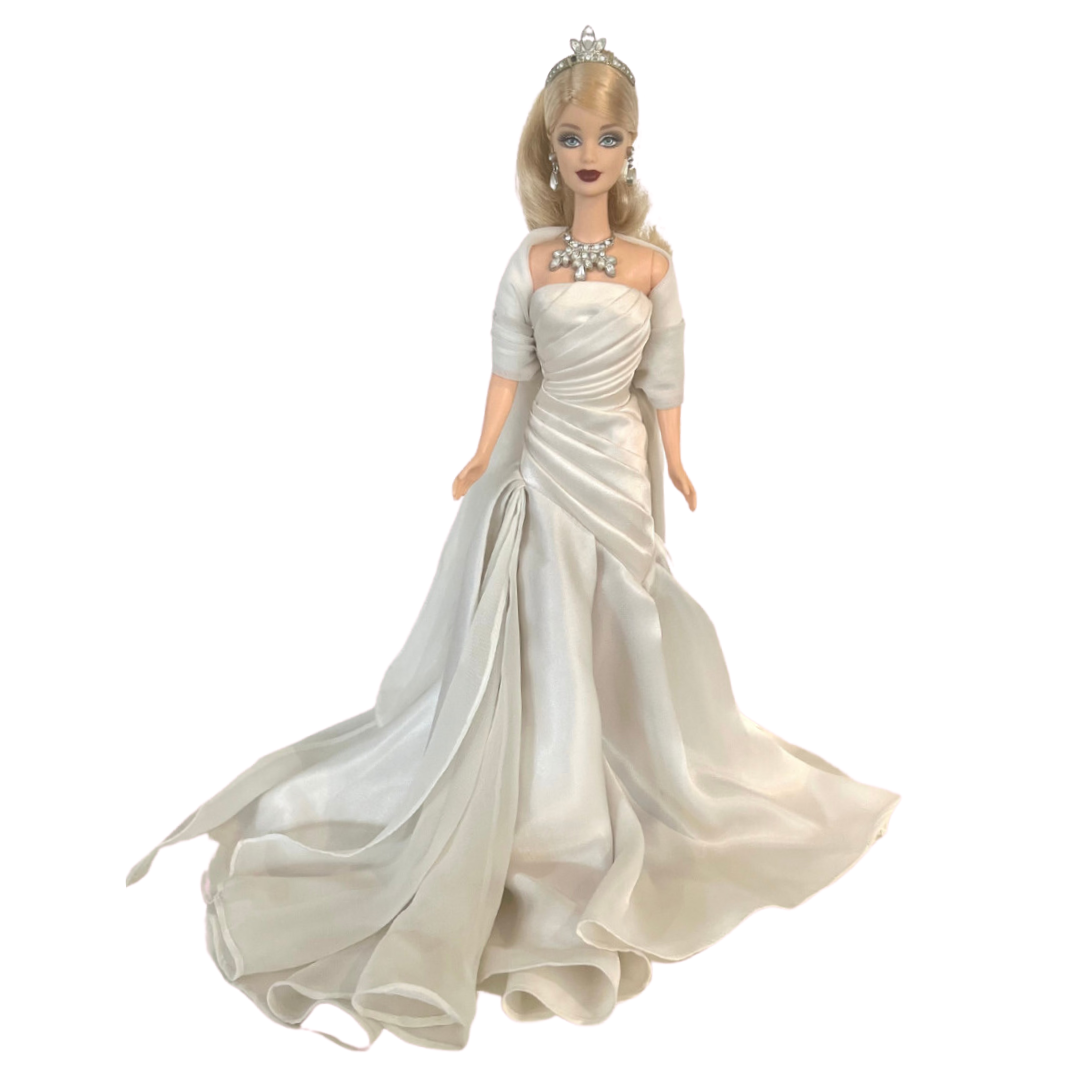 La bambola Duchess of DiamondsTM Barbie si unisce alla compagnia regale nell'acclamata Royal Jewels CollectionTM. Brilla con autentici cristalli chiari e scintillanti, squisitamente incastonati nella sua tiara, collana e orecchini. Il suo lungo abito da sera, in una tonalità perlata di charmeuse bianco, è completato da una stola di chiffon bianco sporco abbinata, che completa elegantemente l'opulento ensemble.