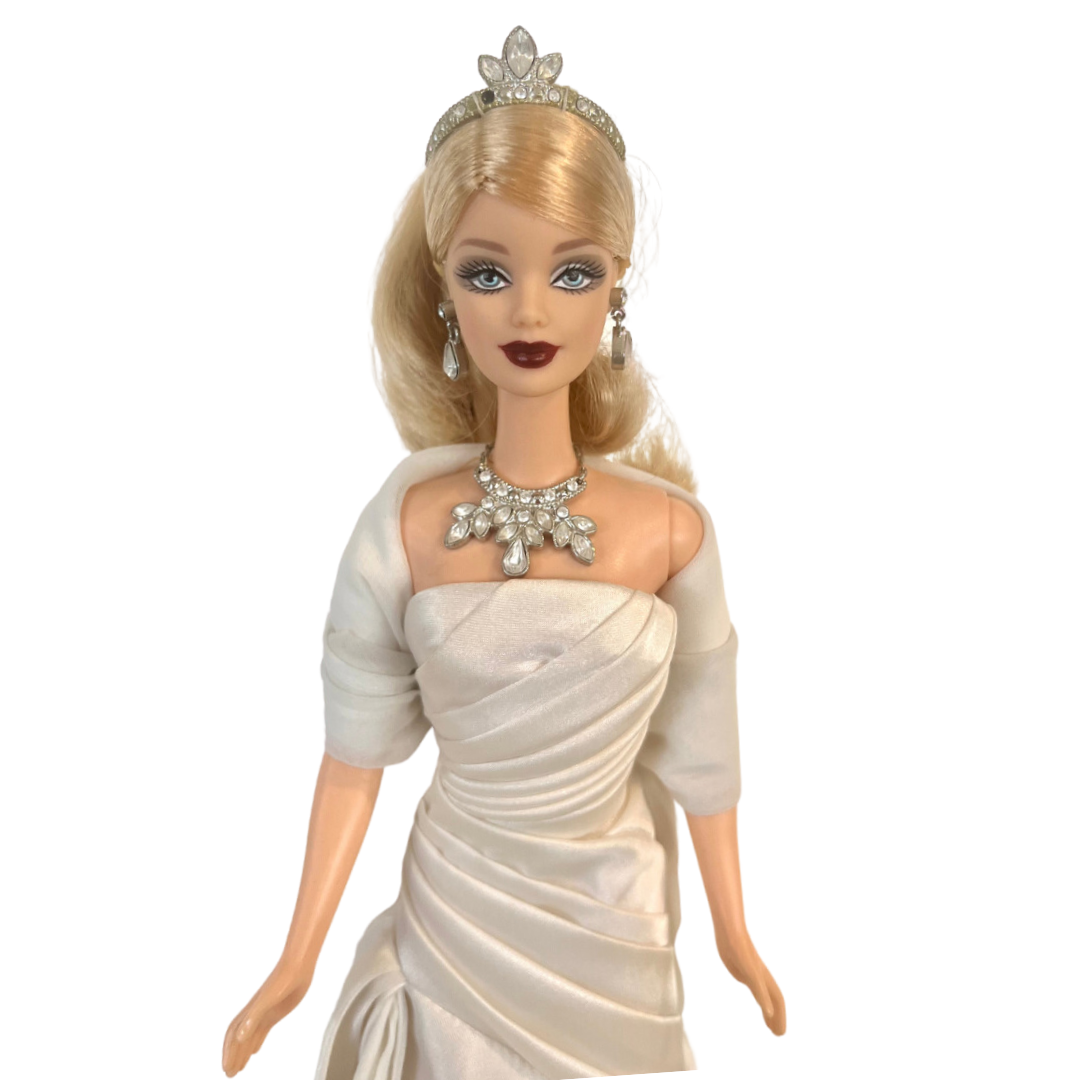 La bambola Duchess of DiamondsTM Barbie si unisce alla compagnia regale nell'acclamata Royal Jewels CollectionTM. Brilla con autentici cristalli chiari e scintillanti, squisitamente incastonati nella sua tiara, collana e orecchini. Il suo lungo abito da sera, in una tonalità perlata di charmeuse bianco, è completato da una stola di chiffon bianco sporco abbinata, che completa elegantemente l'opulento ensemble.