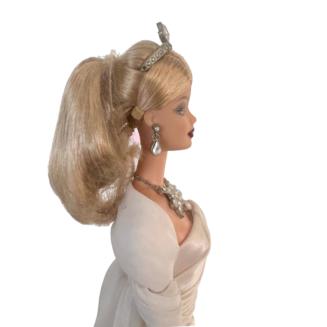 La bambola Duchess of DiamondsTM Barbie si unisce alla compagnia regale nell'acclamata Royal Jewels CollectionTM. Brilla con autentici cristalli chiari e scintillanti, squisitamente incastonati nella sua tiara, collana e orecchini. Il suo lungo abito da sera, in una tonalità perlata di charmeuse bianco, è completato da una stola di chiffon bianco sporco abbinata, che completa elegantemente l'opulento ensemble.
