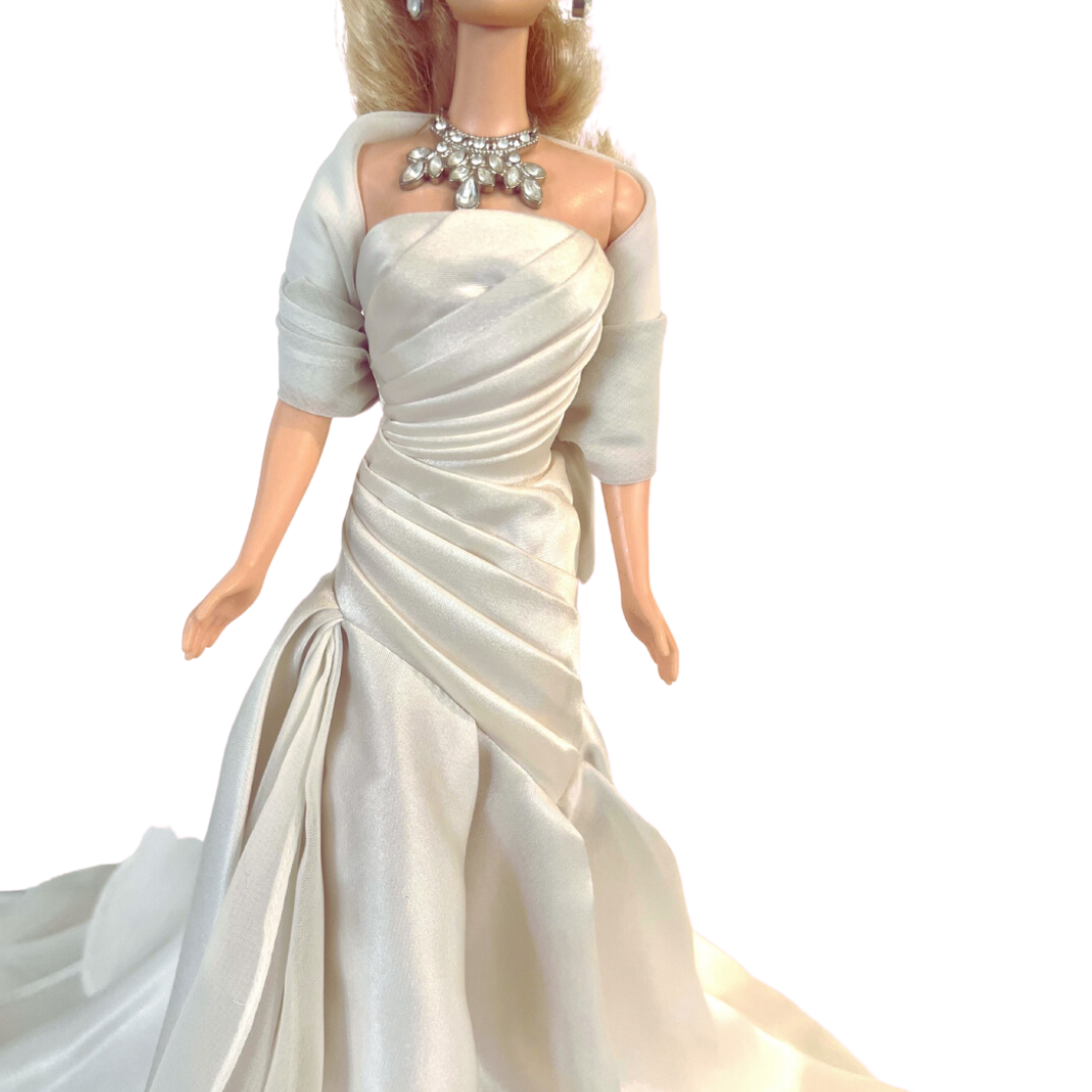 La bambola Duchess of DiamondsTM Barbie si unisce alla compagnia regale nell'acclamata Royal Jewels CollectionTM. Brilla con autentici cristalli chiari e scintillanti, squisitamente incastonati nella sua tiara, collana e orecchini. Il suo lungo abito da sera, in una tonalità perlata di charmeuse bianco, è completato da una stola di chiffon bianco sporco abbinata, che completa elegantemente l'opulento ensemble.