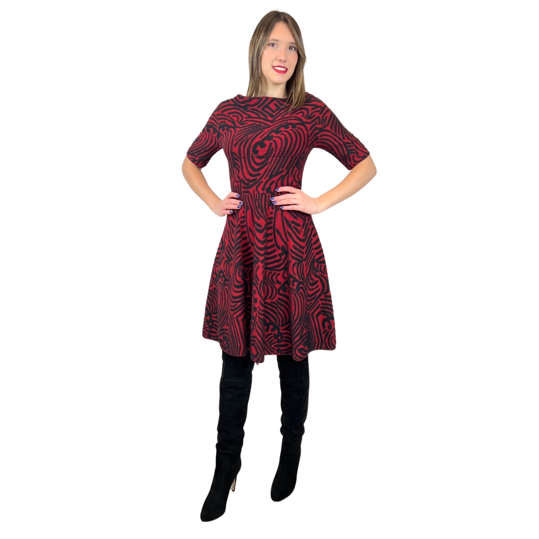 Abito in maglia di lana con fondo nero e con disegni irregolari sui toni del rosso. Collo a barchetta e gonna a ruota, manica a 3/4. Tg. L