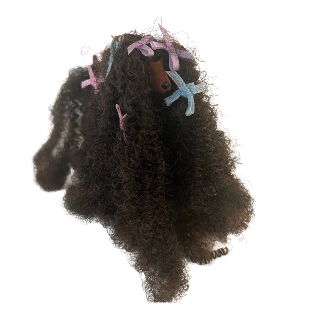 Si dice che il cane assomigli al proprio padrone ed è sicuramente il caso di questa Barbie che ha la chioma identica al pelo del suo animaletto!  Christie Barbie brilla con un abito sottoveste bordato in pizzo viola, con un cardigan coordinato rifinito in pelliccia sintetica viola e sabot viola. Sfoggia splendidi capelli ricci stretti accentati con fiocchi viola per abbinarli al suo vestito. 