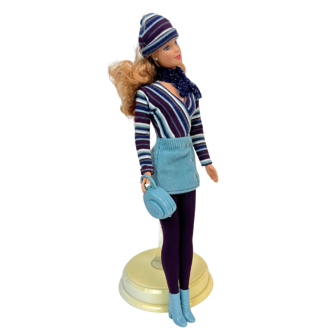  Barbie Corduroy Cool è una produzione Mattel del 1999 ed è una bambola meravigliosa.  Barbie è all'apice della moda dei primi anni 2000; in questa versione la bambola indossa una gonna di velluto a coste verde acqua, una camicia a maniche lunghe a righe marrone, con un berretto sempre rigato  e stivaletti abbinati. 