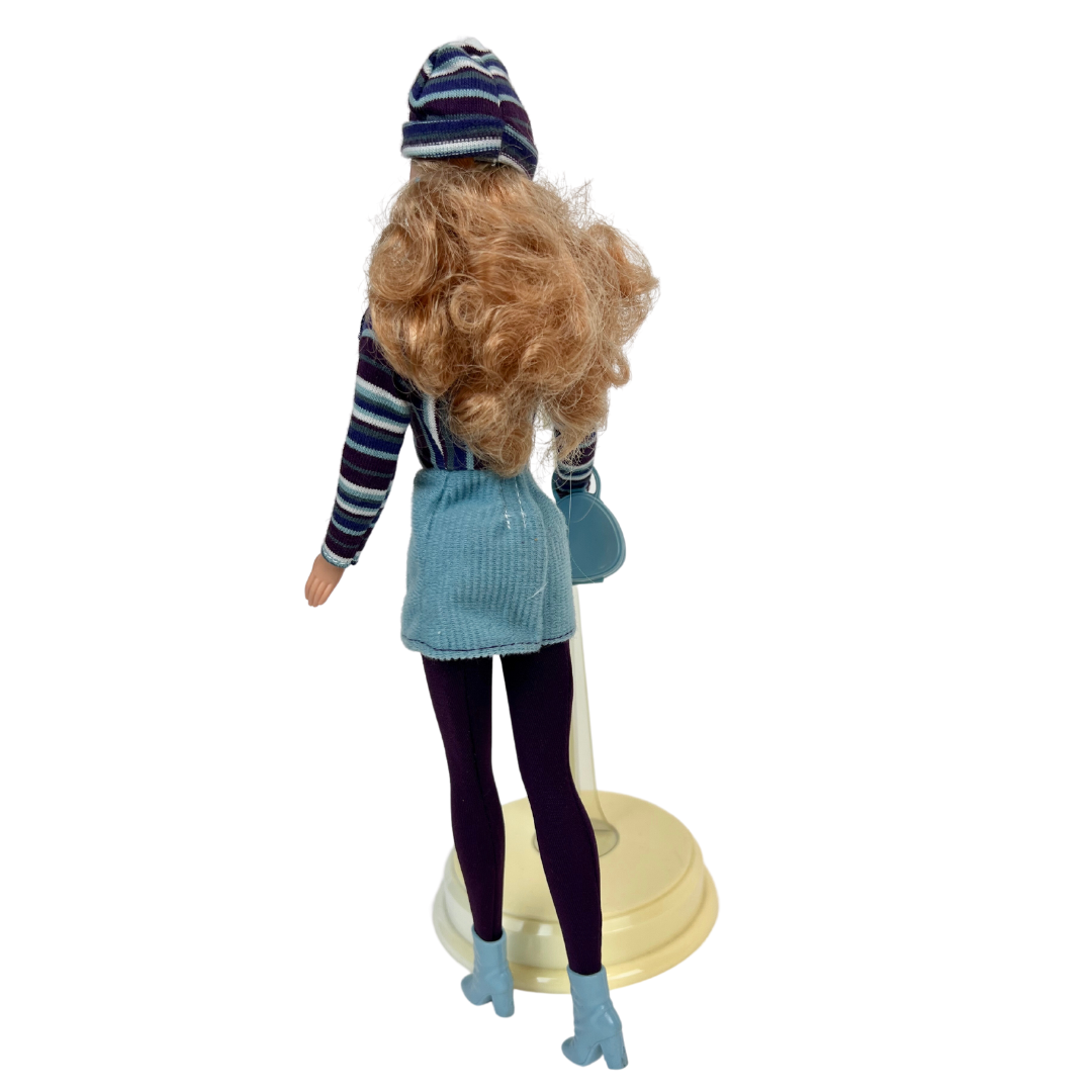  Barbie Corduroy Cool è una produzione Mattel del 1999 ed è una bambola meravigliosa.  Barbie è all'apice della moda dei primi anni 2000; in questa versione la bambola indossa una gonna di velluto a coste verde acqua, una camicia a maniche lunghe a righe marrone, con un berretto sempre rigato  e stivaletti abbinati. 