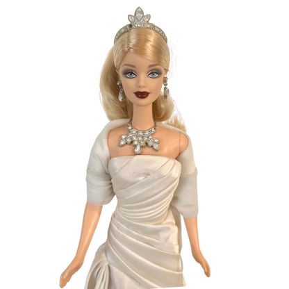 La bambola Duchess of DiamondsTM Barbie si unisce alla compagnia regale nell'acclamata Royal Jewels CollectionTM. Brilla con autentici cristalli chiari e scintillanti, squisitamente incastonati nella sua tiara, collana e orecchini. Il suo lungo abito da sera, in una tonalità perlata di charmeuse bianco, è completato da una stola di chiffon bianco sporco abbinata, che completa elegantemente l'opulento ensemble.