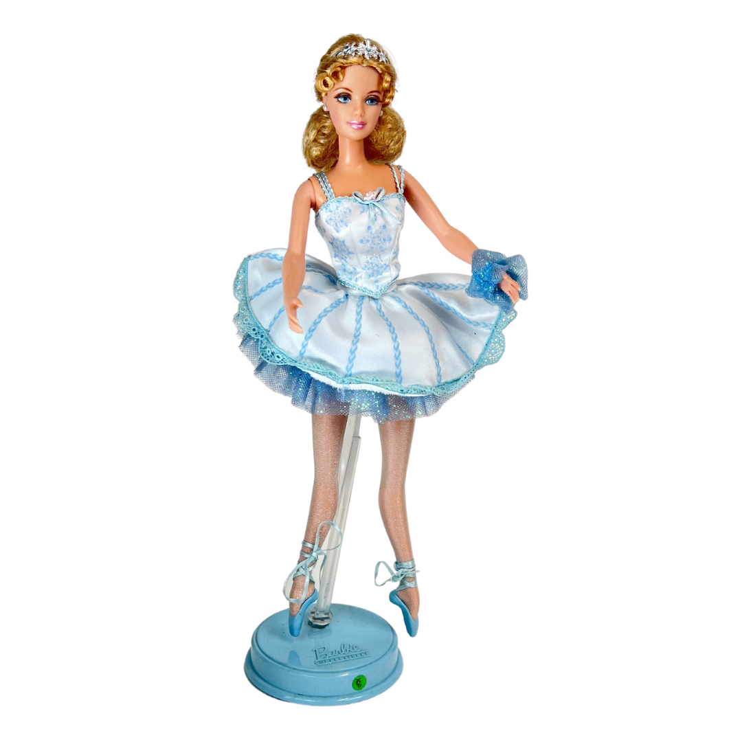 Barbie mozzafiato nel costume da ballerina in raso bianco e tulle blu che brilla di fiocchi di neve e glitter; indossa collant luccicanti e ballerine con lacci e punta blu.  Sfoggia degli orecchini a bottone bianco ma il suo tocco piu' affascinante è una graziosa coroncina argentata portata nei suoi graziosi capelli biondi.