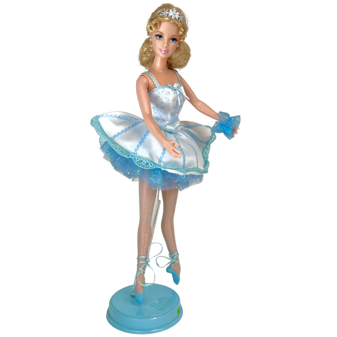 Barbie mozzafiato nel costume da ballerina in raso bianco e tulle blu che brilla di fiocchi di neve e glitter; indossa collant luccicanti e ballerine con lacci e punta blu.  Sfoggia degli orecchini a bottone bianco ma il suo tocco piu' affascinante è una graziosa coroncina argentata portata nei suoi graziosi capelli biondi.