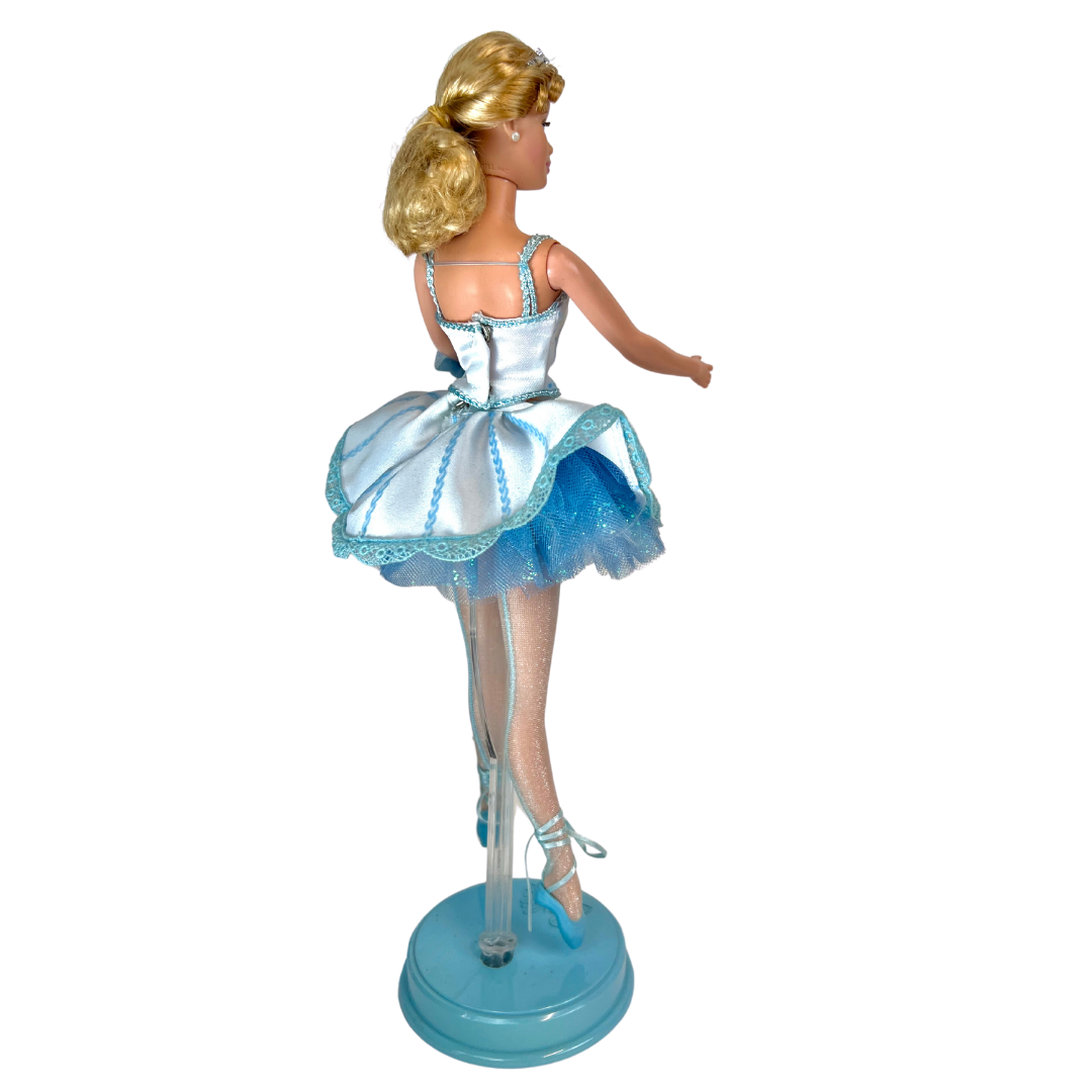 Barbie mozzafiato nel costume da ballerina in raso bianco e tulle blu che brilla di fiocchi di neve e glitter; indossa collant luccicanti e ballerine con lacci e punta blu.  Sfoggia degli orecchini a bottone bianco ma il suo tocco piu' affascinante è una graziosa coroncina argentata portata nei suoi graziosi capelli biondi.