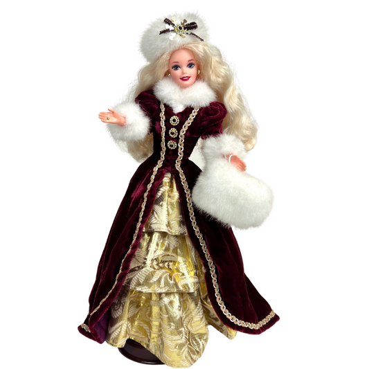  La bambola Barbie Buone Feste, Edizione Speciale è una produzione Mattel del 1996.  Include: bambola Barbie da 11,5", abito bordeaux con finiture in pelliccia sintetica, cappello e manicotto in pelliccia sintetica, sottogonna in broccato dorato, anello, orecchini, scarpe e supporto per bambola da esposizione. Edizione perfetta per la tua collezione Barbie.