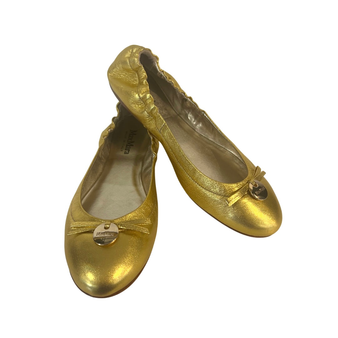 Ballerine in pelle oro metallizzata, punta stondata e elastico sul tallone, piccolo fiocco con medaglietta tonda con logo